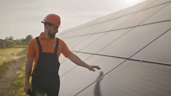 Portrett av en lykkelig mannlig ingeniør i beskyttelseshjelm. Han snakker på en walkie-talkie mens han ser på kamera. Kjekk mann i uniform som smiler mens han står på solenergifarmen. Begrepet grønn energi – stockfoto