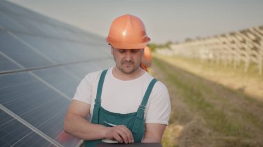 Güneş enerjisi kurulumundaki panelleri kontrol eden güneş panelleri alanında yürüyen teknisyen ve yatırımcı. Elektrik santrali çalışanları ve güneş panelleri şeması hakkında konuşuyorlar..