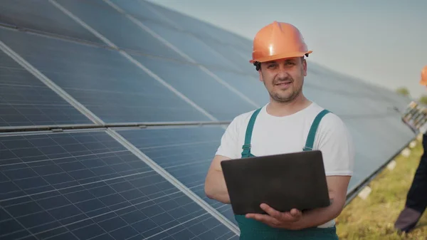 Insinööri seisoo aurinkokenno paneelit etsivät näytön sähkö arvo valmistettu aurinkokennoa. Mies pitää kannettavaa kädessään ja seisoo kentällä aurinkopaneeleilla. Aurinkoenergia — kuvapankkivalokuva