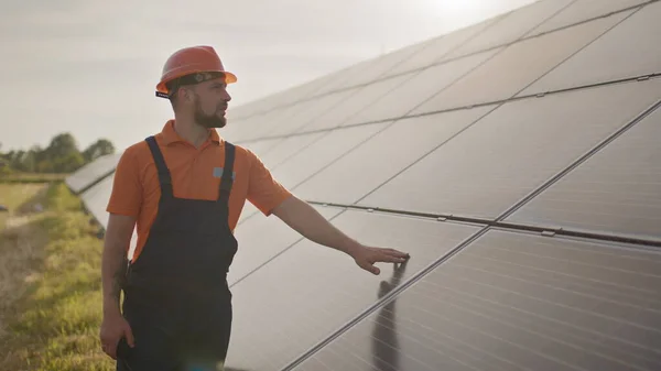 Portrett av en lykkelig mannlig ingeniør i beskyttelseshjelm. Han snakker på en walkie-talkie mens han ser på kamera. Kjekk mann i uniform som smiler mens han står på solenergifarmen. Begrepet grønn energi – stockfoto