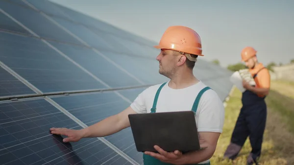 Inženýr stojící se solárními panely a sledující monitor hodnoty elektrické energie vyrobené ze solárního článku. Muž držící notebook v rukou, stojící na hřišti se solárními panely. Solární energie — Stock fotografie