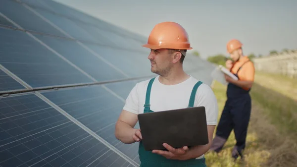 Ingeniør står med solcellepaneler og ser på strømverdien fra solcellen. Mannen som holder laptopen i hendene sine stående på jorder med solcellepaneler. Solenergi – stockfoto