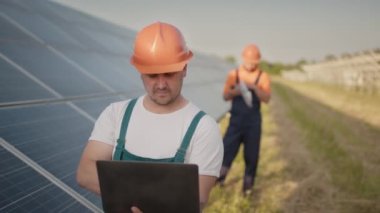 Güneş enerjisi kurulumundaki panelleri kontrol eden güneş panelleri alanında yürüyen teknisyen ve yatırımcı. Elektrik santrali çalışanları ve güneş panelleri şeması hakkında konuşuyorlar..