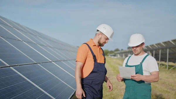 Coworking ingeniører på solkraftverk. Voksne menn i hatt, en ansatt i et kraftverk sender kommandoer via walkie-talkie. Transport av ren energi. Ren energi. Solfylte batterier. – stockfoto