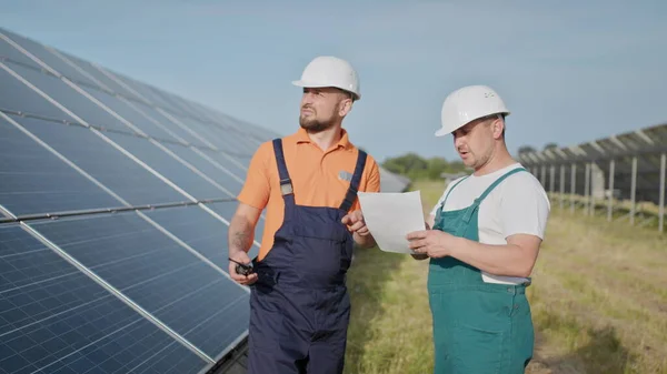 Aurinkovoimalan insinöörit. Aikuiset miehet kypärissä, Voimalaitoksen työntekijä lähettää käskyjä radiopuhelimella. Puhtaan energian kuljetus. Puhdasta energiaa. Aurinkoparistot. — kuvapankkivalokuva