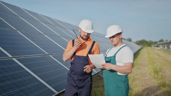 Coworking ingeniører på solkraftverk. Voksne menn i hatt, en ansatt i et kraftverk sender kommandoer via walkie-talkie. Transport av ren energi. Ren energi. Solfylte batterier. – stockfoto