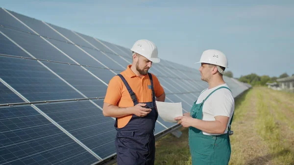 에너지 기술자가 태양 전지 패널을 점검하는 태양 농장 에너지. 태양 에너지는 태양 에너지 역수를 거쳐 공장의 전기로 바뀝니다. 발전소 직원 이 워키토키의 명령을 전달하는 모습. — 스톡 사진