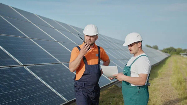 Energian teknikko tarkistaa aurinkokennojen paneelit aurinkoenergialla. Aurinkoenergiaa Sun invertteri Sähkö Factory. Voimalaitoksen työntekijä lähettää käskyjä radiopuhelimella. — kuvapankkivalokuva