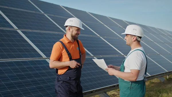 에너지 기술자가 태양 전지 패널을 점검하는 태양 농장 에너지. 태양 에너지는 태양 에너지 역수를 거쳐 공장의 전기로 바뀝니다. 발전소 직원 이 워키토키의 명령을 전달하는 모습. — 스톡 사진
