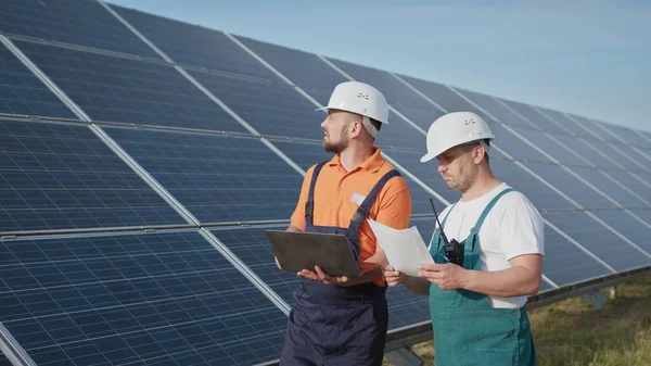能源专家使用数字平板读数信息来检查太阳能电池板的建造效率。绿色能源工作。技术。两名太阳能发电厂工人正在记录数据 — 图库照片