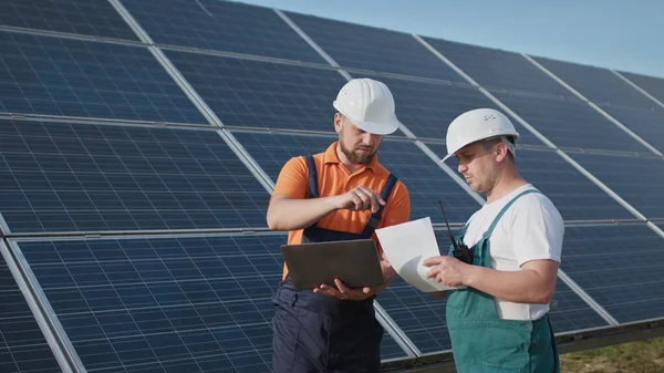 Energy specialist using digital tablet reading information to check the efficiency of solar panel construction. Green energy jobs. Technology. Two solar power plant workers are recording data