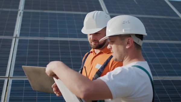 Lähikuva insinöörit käyttävät kannettavaa tietokonetta ja projektisuunnitelma aurinkopaneeli erityinen yhtenäinen seisoo katsoa ympärilleen keskustella asennus aurinkoinen akkujen sähkön ympäristöön. Vihreän energian työpaikat — kuvapankkivalokuva