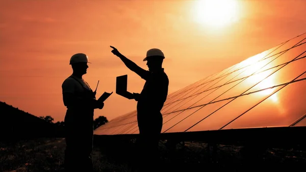 To uidentifiserte solenergiingeniører i baklys ved solnedgang. Kolleger i industrien bruker overvåkningsrekker på nettbrett med solcellepaneler ved solnedgang. Solpark. Alternativt energibegrep – stockfoto