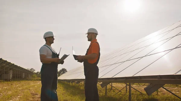 Kolleger i industrien bruker overvåkningsrekker på nettbrett med solcellepaneler ved solnedgang. Forretningssamarbeid. Solpark. Alternativt energibegrep. Solcelleanlegg. – stockfoto