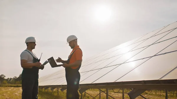 Kolleger i industrien bruker overvåkningsrekker på nettbrett med solcellepaneler ved solnedgang. Forretningssamarbeid. Solpark. Alternativt energibegrep. Solcelleanlegg. – stockfoto