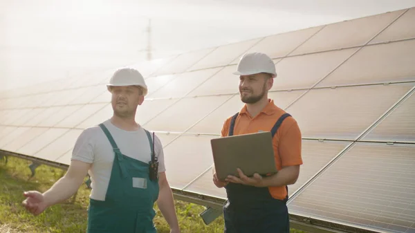 Miesinsinöörit seisomassa aurinkotilalla ja keskustelemassa tehokkaasta rakennussuunnitelmasta. Kaksi miestä suojakypärässä. Insinööri pitää kätensä ilmassa, paikka virtuaalinen näytönsäästäjä. — kuvapankkivalokuva