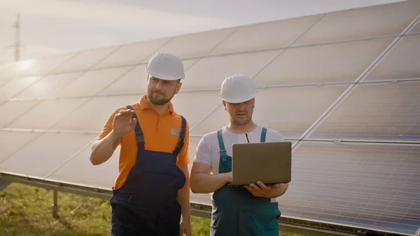 Ingeniøren holder hånden i luften, et sted for en virtuell skjermsparer. Mannlige ingeniører som står på solfarmen og diskuterer effektive byggeplaner. To menn i beskyttelseshjelm. – stockfoto