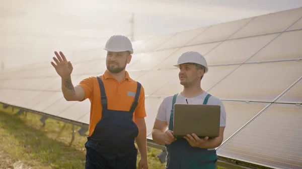 Ingeniøren holder hånden i luften, et sted for en virtuell skjermsparer. Mannlige ingeniører som står på solfarmen og diskuterer effektive byggeplaner. To menn i beskyttelseshjelm. – stockfoto