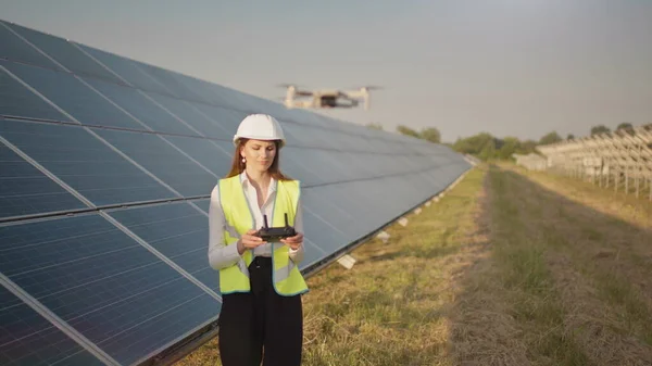 Inżynierka w twardym kapeluszu trzymająca tablet, obsługująca latające drony w elektrowniach słonecznych. Instalacja panelu fotowoltaicznego. Układ słoneczny. Nowe technologie. — Zdjęcie stockowe