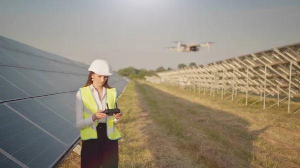 Inżynierka w twardym kapeluszu trzymająca tablet, obsługująca latające drony w elektrowniach słonecznych. Instalacja panelu fotowoltaicznego. Układ słoneczny. Nowe technologie. — Zdjęcie stockowe