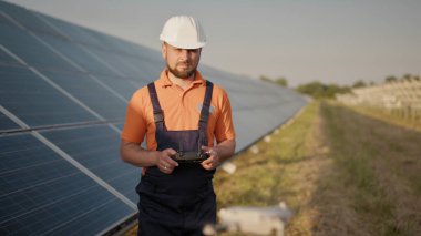 Fotovoltaik güneş enerjisi santralinde kask takan ve insansız hava aracını kontrol eden bir endüstri uzmanı. Güneş paneli kurulumu. Teknoloji ve ekoloji. Yeni teknolojiler
