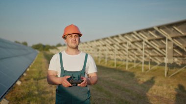 Bir güneş enerjisi santralinin çalışanı bir telsizle konuşurken meslektaşları ve bir yatırımcı güneş enerjisi santralini kızılötesi tarayıcı, bir İHA ile kontrol ediyorlar. İHA mühendisi portresi