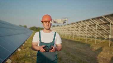 Bir güneş enerjisi santralinin çalışanı bir telsizle konuşurken meslektaşları ve bir yatırımcı güneş enerjisi santralini kızılötesi tarayıcı, bir İHA ile kontrol ediyorlar. İHA mühendisi portresi