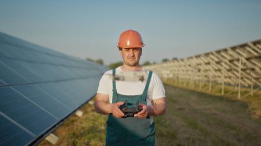 Bir güneş enerjisi santralinin çalışanı bir telsizle konuşurken meslektaşları ve bir yatırımcı güneş enerjisi santralini kızılötesi tarayıcı, bir İHA ile kontrol ediyorlar. İHA mühendisi portresi