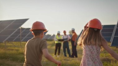 İki küçük çocuk iş yerindeki ebeveynlerine koşuyor. İş yerinde çocukları kameraya gülümseyen bir güneş enerjisi santrali çalışanı. Bir güneş enerjisi tesisinde üç güneş enerjisi uzmanı..