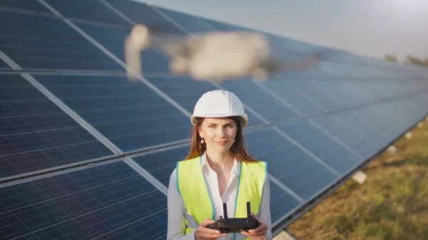 Portrett av en kvinnelig ingeniør som opererer en drone på bakgrunn av et solkraftverk. Solpaneloppstilling. Teknologi og økologi. Solnedgang. – stockfoto