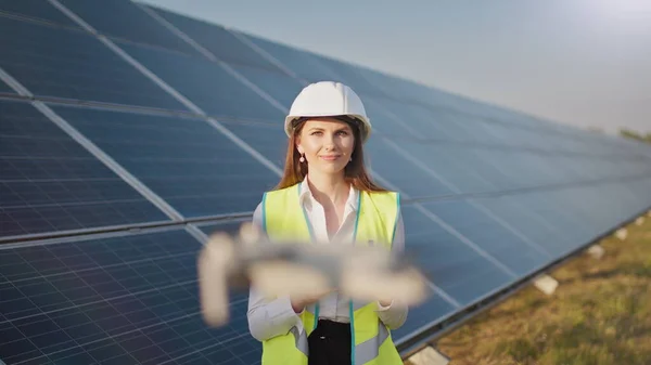 Portrett av en kvinnelig ingeniør som opererer en drone på bakgrunn av et solkraftverk. Solpaneloppstilling. Teknologi og økologi. Solnedgang. – stockfoto