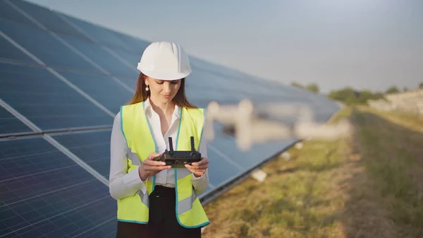 Portrett av en kvinnelig ingeniør som opererer en drone på bakgrunn av et solkraftverk. Solpaneloppstilling. Teknologi og økologi. Solnedgang. – stockfoto