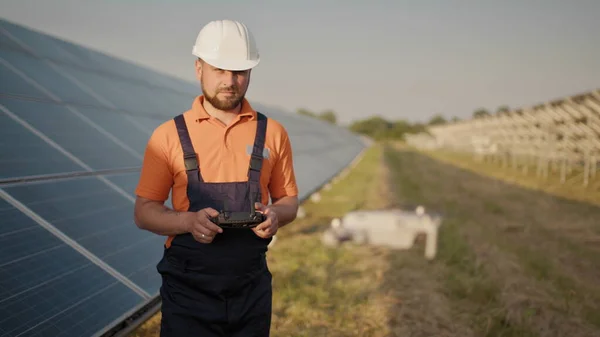 Teollisuuden asiantuntija yllään kypärä ja ohjaus drone aurinkosähkövoimalassa. Aurinkopaneelien asennus. Teknologiat ja ekologia. Uudet teknologiat — kuvapankkivalokuva