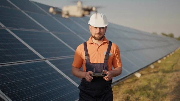 Industrial expert wearing helmet and controlling drone in photovoltaic solar power plant. Solar panel array installation. Technologies and ecology. New technologies