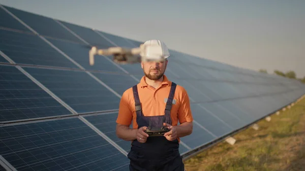 Teollisuuden asiantuntija yllään kypärä ja ohjaus drone aurinkosähkövoimalassa. Aurinkopaneelien asennus. Teknologiat ja ekologia. Naissijoittaja tarkastaa työn — kuvapankkivalokuva