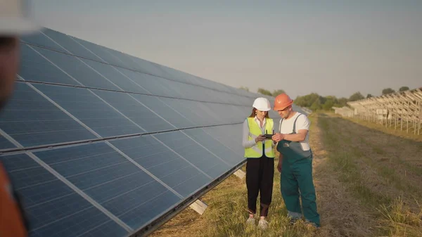 En ansatt ved et solkraftverk snakker på en walkie-talkie, mens kollegaene og investorene sjekker solkraftverket med en infrarød skanner, en drone. Installasjon av solcellepaneler – stockfoto