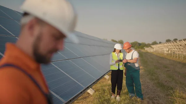 En ansatt ved et solkraftverk snakker på en walkie-talkie, mens kollegaene og investorene sjekker solkraftverket med en infrarød skanner, en drone. Installasjon av solcellepaneler – stockfoto