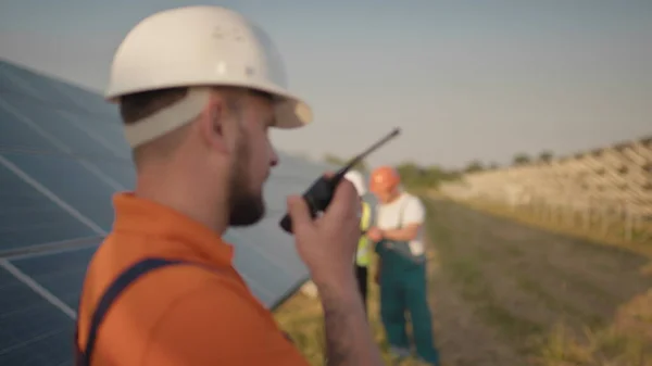 Un angajat al unei centrale solare vorbește despre un walkie-talkie în timp ce colegii săi și un investitor verifică centrala solară cu un scaner infraroșu, o dronă. Instalare panou solar fotovoltaic — Fotografie, imagine de stoc