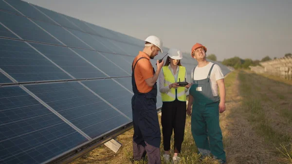 An employee of a solar power plant talks on a walkie-talkie while his colleagues and an investor check the solar power plant with an infrared scanner, a drone. Photovoltaic solar panel installation