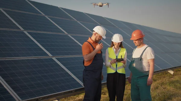 Aurinkovoimalan työntekijä puhuu radiopuhelimella, kun hänen kollegansa ja sijoittaja tarkistavat aurinkovoimalan infrapunaskannerilla, droonilla. Aurinkosähköpaneelien asennus — kuvapankkivalokuva