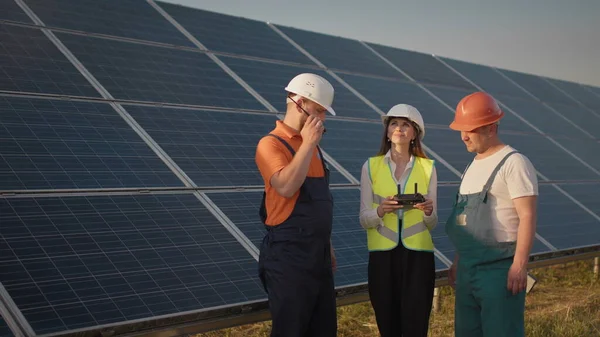 Um funcionário de uma usina de energia solar fala em um walkie-talkie enquanto seus colegas e um investidor verificam a usina de energia solar com um scanner infravermelho, um drone. Instalação do painel solar fotovoltaico — Fotografia de Stock