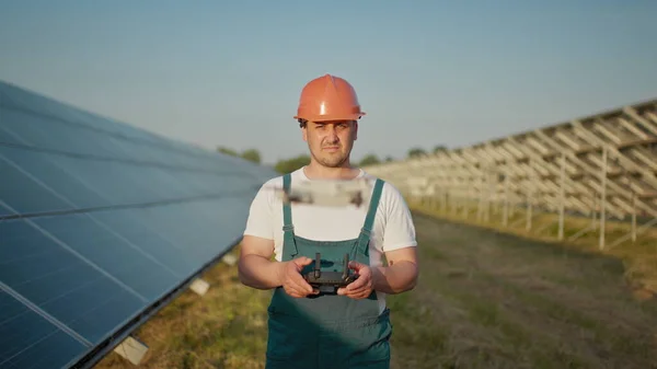En ansatt ved et solkraftverk snakker på en walkie-talkie, mens kollegaene og investorene sjekker solkraftverket med en infrarød skanner, en drone. Portrett av dronetekniker – stockfoto
