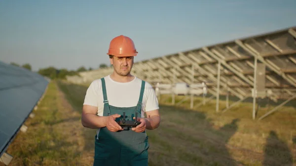 En ansatt ved et solkraftverk snakker på en walkie-talkie, mens kollegaene og investorene sjekker solkraftverket med en infrarød skanner, en drone. Portrett av dronetekniker – stockfoto