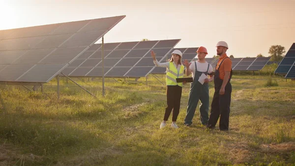 Business team of industrial technicians walking through solar park outside. Construction of concentrated solar power plant. Renewable energy. Ecology. Technician and investor checking the solar panels