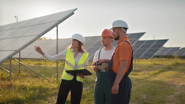 Kolme aurinkoenergian asiantuntijaa aurinkovoimalassa. Ammattitaitoiset insinöörit keskustelevat innovatiivisesta hankkeesta. Teollisuusteknikoiden tiimi aurinkopuistossa. Aurinkovoimalan rakentaminen. — kuvapankkivalokuva