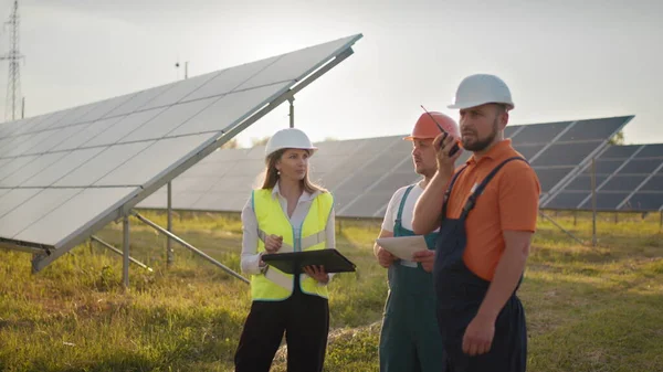 Tre spesialister på solenergi ved et solkraftverk. Profesjonelle ingeniører diskuterer innovativt prosjekt. Industriteknikere i solparken. Bygging av solkraftverk. – stockfoto