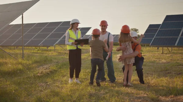 Kolme aurinkoenergian asiantuntijaa aurinkovoimalassa. Kaksi pientä lasta juoksee vanhemmilleen, jotka ovat töissä. Aurinkovoimalan työntekijä, jolla on työssä lapsia ja joka hymyilee kameralle. Onnellinen — kuvapankkivalokuva