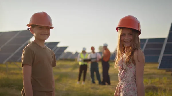 Duas crianças pequenas correm para os pais que estão no trabalho. Um funcionário da usina solar com crianças no trabalho sorrindo para a câmera. Três especialistas em energia solar em uma usina de energia solar. — Fotografia de Stock
