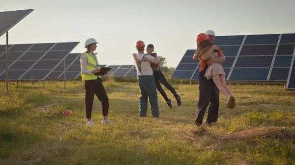 Kaksi pientä lasta juoksee vanhemmilleen, jotka ovat töissä. Aurinkovoimalan työntekijä, jolla on työssä lapsia ja joka hymyilee kameralle. Kolme aurinkoenergian asiantuntijaa aurinkovoimalassa. — kuvapankkivalokuva