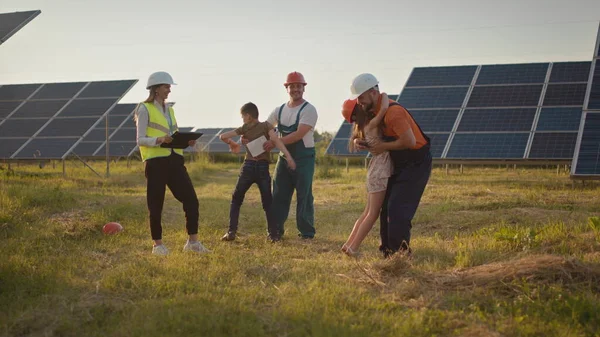 Two small children run to their parents who are at work. A solar power plant employee with children at work smiling at the camera. Three solar energy specialists at a solar power facility.